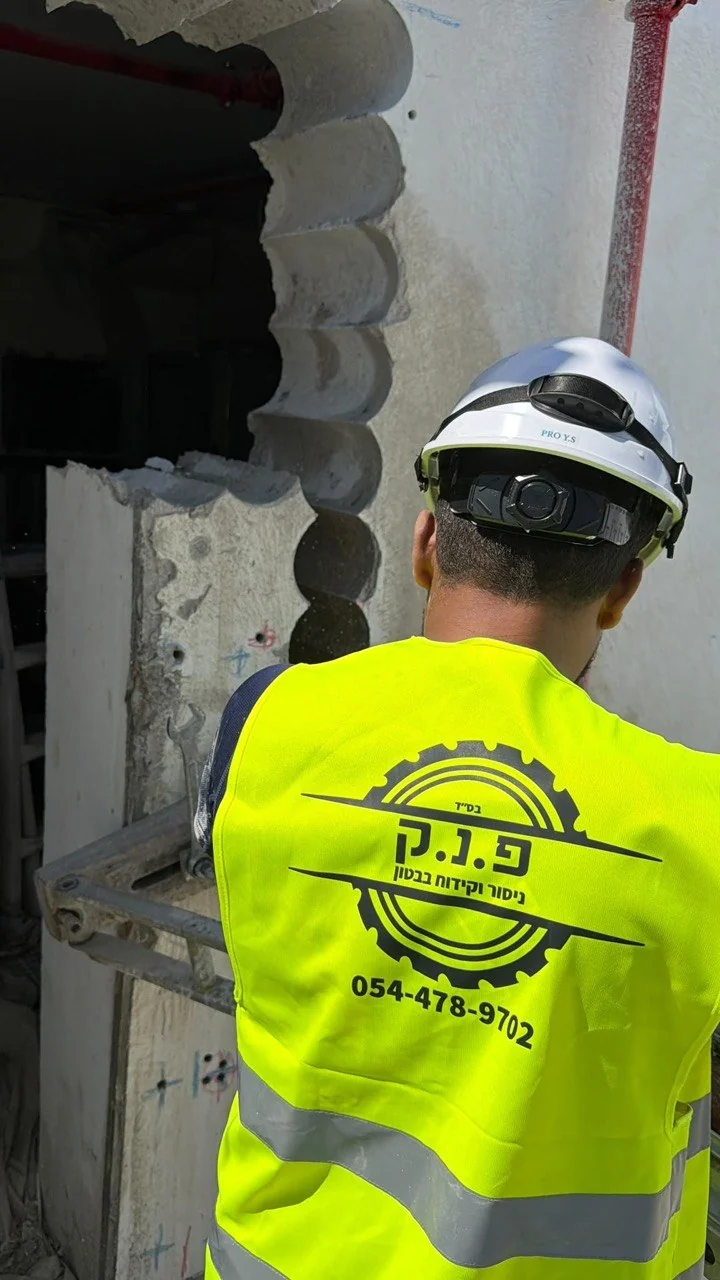 עובד עם אפוד פ.נ.ק מול פתח בקיר בטון